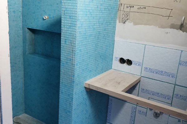 Badezimmer mit blauen Mosaikfliesen, einer Nische und einem Holzregal, teilweise renoviert.