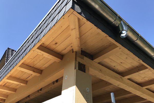 Dachüberstand mit Holzunterkonstruktion und Schieferdeckung unter blauem Himmel.