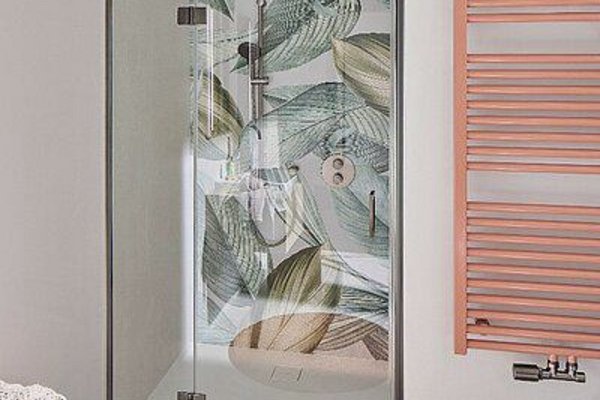 Moderne Dusche mit Glasabtrennung und Pflanzenmuster, daneben ein Handtuchhalter in Rosé und ein Waschbecken.
