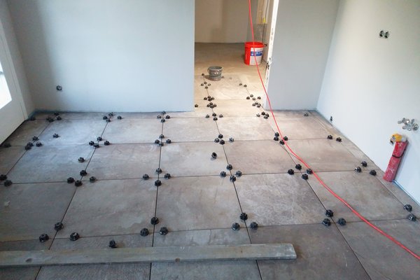Fliesenarbeiten in einem Raum mit verlegten Fliesen und Abstandhaltern, Kabel und Werkzeug sichtbar.