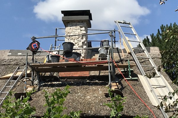 Sanierungsarbeiten an einem Reetdach mit Gerüst, Leitern und Baumaterialien.