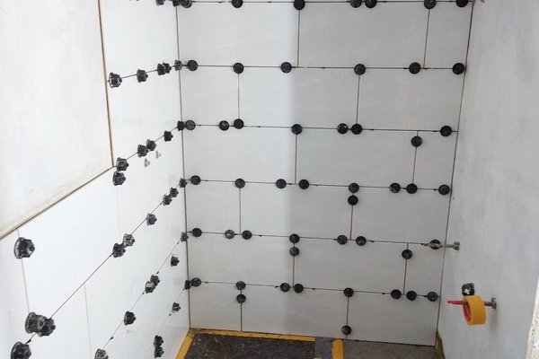 Fliesenarbeiten in einem Badezimmer mit verlegten Fliesen und Abstandshaltern an der Wand.