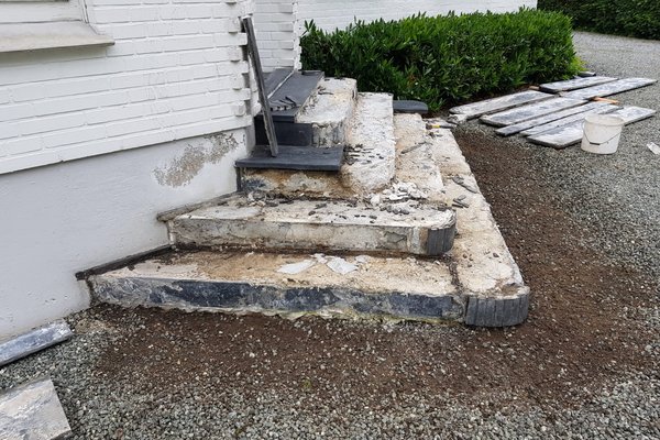 Abgeplatzte Treppe mit unebenen Stufen und Baustellenmaterialien im Hintergrund, bereit für Sanierungsarbeiten.