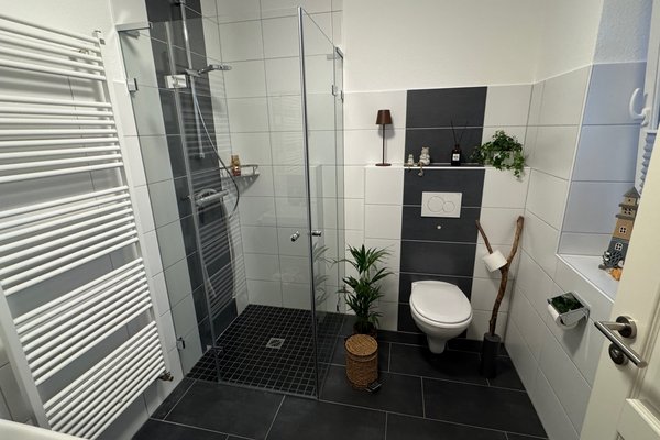 Modernes Badezimmer mit Dusche, WC, Handtuchheizkörper und Pflanzen in neutralen Farben.