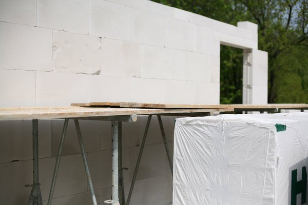 Mauerwerk aus weißen Blöcken mit Gerüst und Holzplatte für Maurerarbeiten.