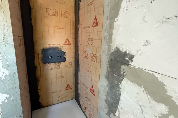 Sanierter Duschbereich mit gefliester Wand und Duschwanne, bereit für die Fliesenarbeiten.