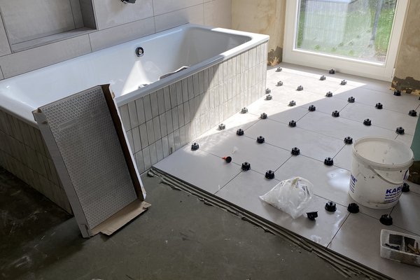 Badezimmer mit Badewanne und verlegten Fliesen, Baustelle mit Fliesenmaterial und Werkzeugen.