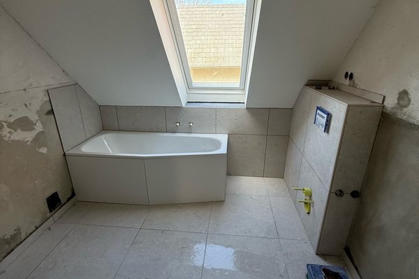 Modernes Badezimmer mit freistehender Badewanne, großen Fliesen und Dachfenster. Wände teilweise unvollständig.