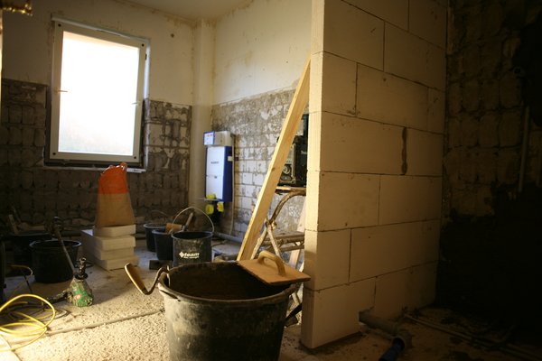 Sanierungsarbeiten in einem Raum mit unvollständiger Wand, Baustellenmaterialien und Werkzeugen.