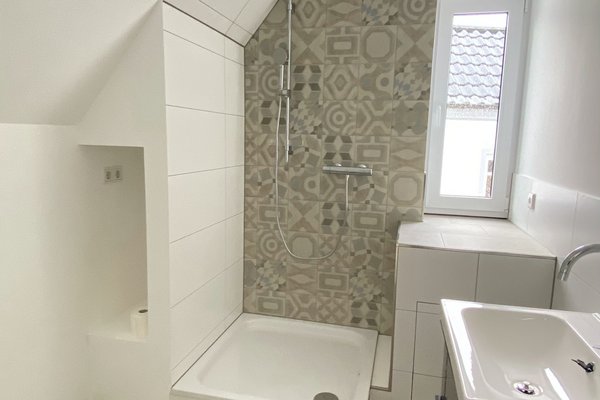 Modernes Badezimmer mit Dusche, Waschbecken und dekorativer Wandfliese. Helle, freundliche Atmosphäre.