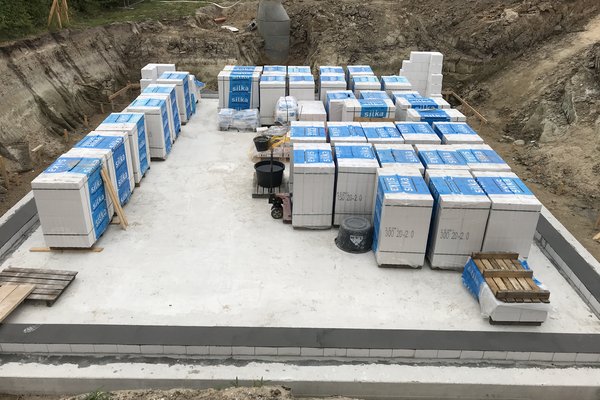 Lagerplatz mit gestapelten Baustellenmaterialien auf einem betonierten Fundament in einer Baugrube.
