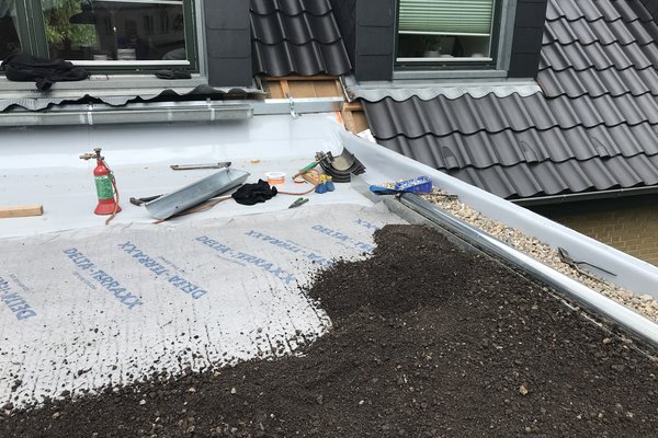 Dachfläche mit Schotter und Materialien für die Abdichtung, Fenster im Hintergrund.
