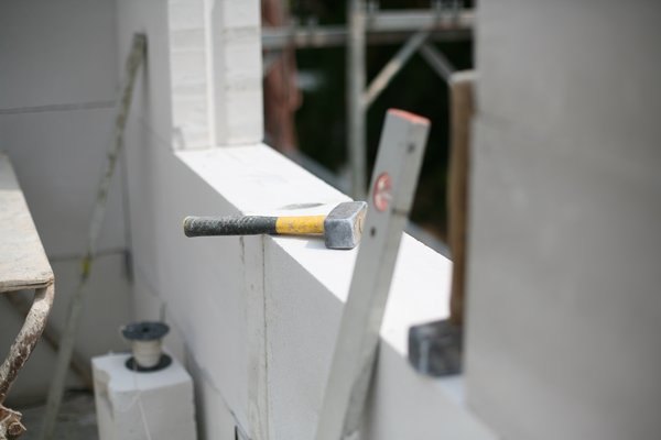 Ein Hammer und eine Wasserwaage liegen auf einer Mauer, umgeben von Baustellenmaterialien.