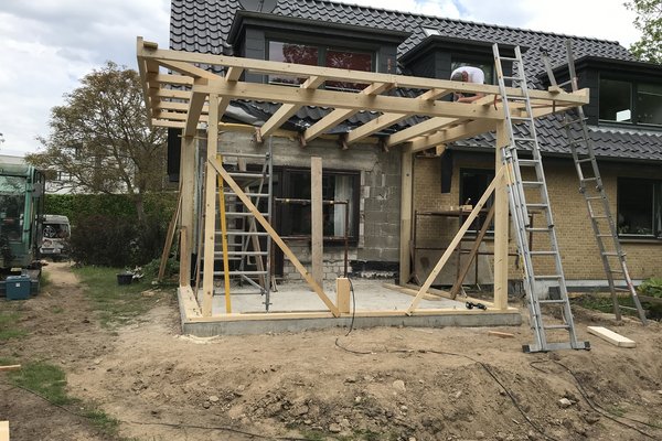 Holzgerüst für einen Anbau an einem Wohnhaus, mit Leitern und Baustellenmaterial im Garten.