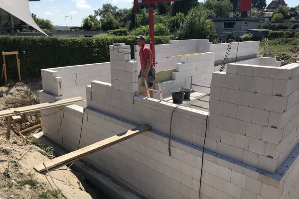 Maurerarbeiten an einem Rohbau mit weißen Blocksteinen und einem Kran im Hintergrund.