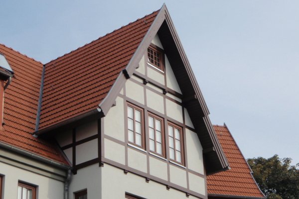 Fachwerkhaus mit rotem Satteldach und mehreren Fenstern, umgeben von Bäumen.