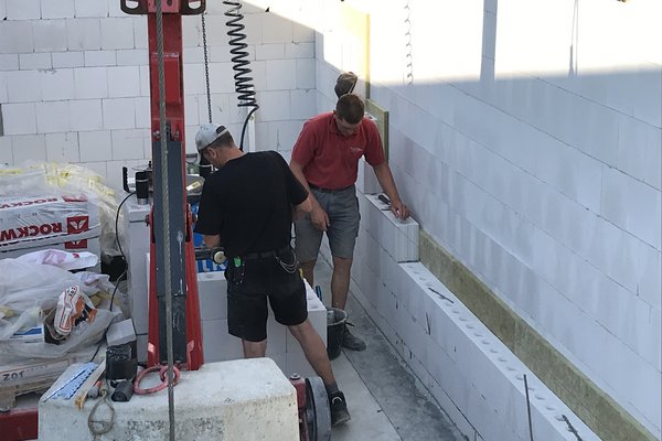 Maurerarbeiten an einer Wand mit weißen Blöcken, Handwerker arbeiten mit Werkzeug und Material auf einer Baustelle.