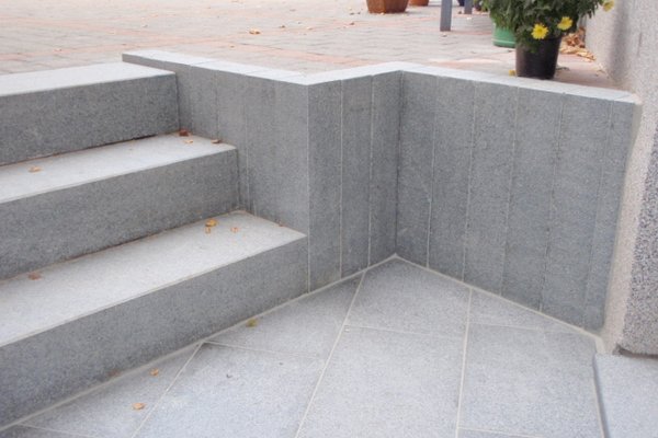 Graue Steinplatten bilden eine Treppe mit einer Ecke, die sorgfältig verlegt und verarbeitet ist.