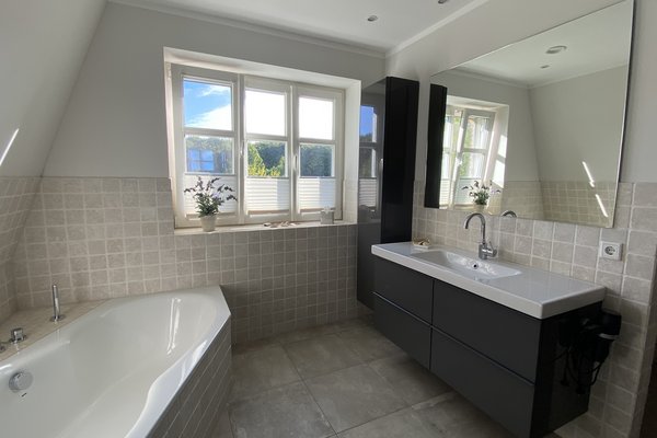 Modernes Badezimmer mit Badewanne, Waschbecken und großen Fenstern für viel Tageslicht.