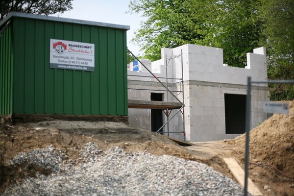 Bauarbeiten mit einem Rohbau aus weißen Steinen und einem grünen Baucontainer im Vordergrund.