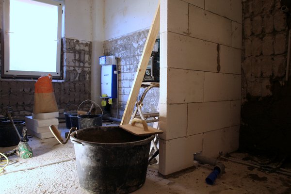 Bauarbeiten in einem Raum mit Mauerwerk, Eimer, Werkzeug und Baustellenmaterialien.
