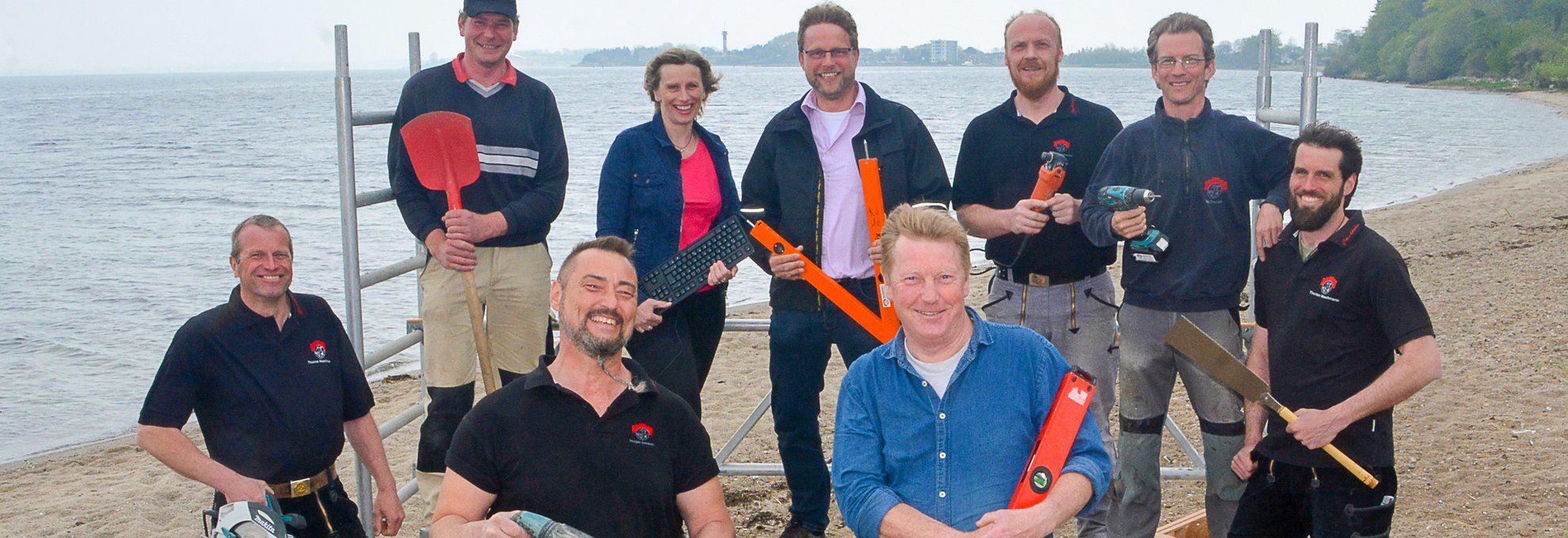 Das Strohbehn Handwerker-Team am Strand mit Werkzeugen, bereit für Bau- und Sanierungsarbeiten in der Umgebung.