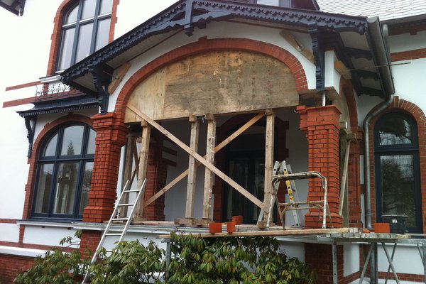 Sanierungsarbeiten an einem Eingangsbereich mit Gerüst, Holzstützen und einer provisorischen Wand.
