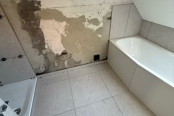 Sanierter Badezimmerbereich mit freiliegender Wand, Badewanne und Fliesenboden.