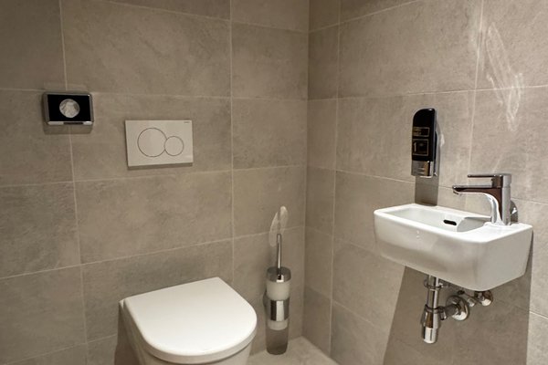 Modernes Badezimmer mit grauen Fliesen, WC und kleinem Waschbecken.