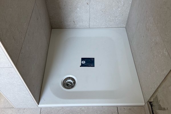 Duschwanne aus weißem Material, umgeben von hellen Fliesen, bereit für die Installation.