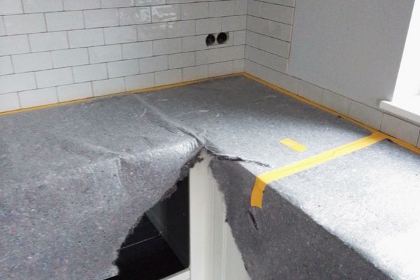 Arbeitsfläche in einer Küche mit abgedecktem Bereich, umgeben von weißen Fliesen und Küchenschränken.